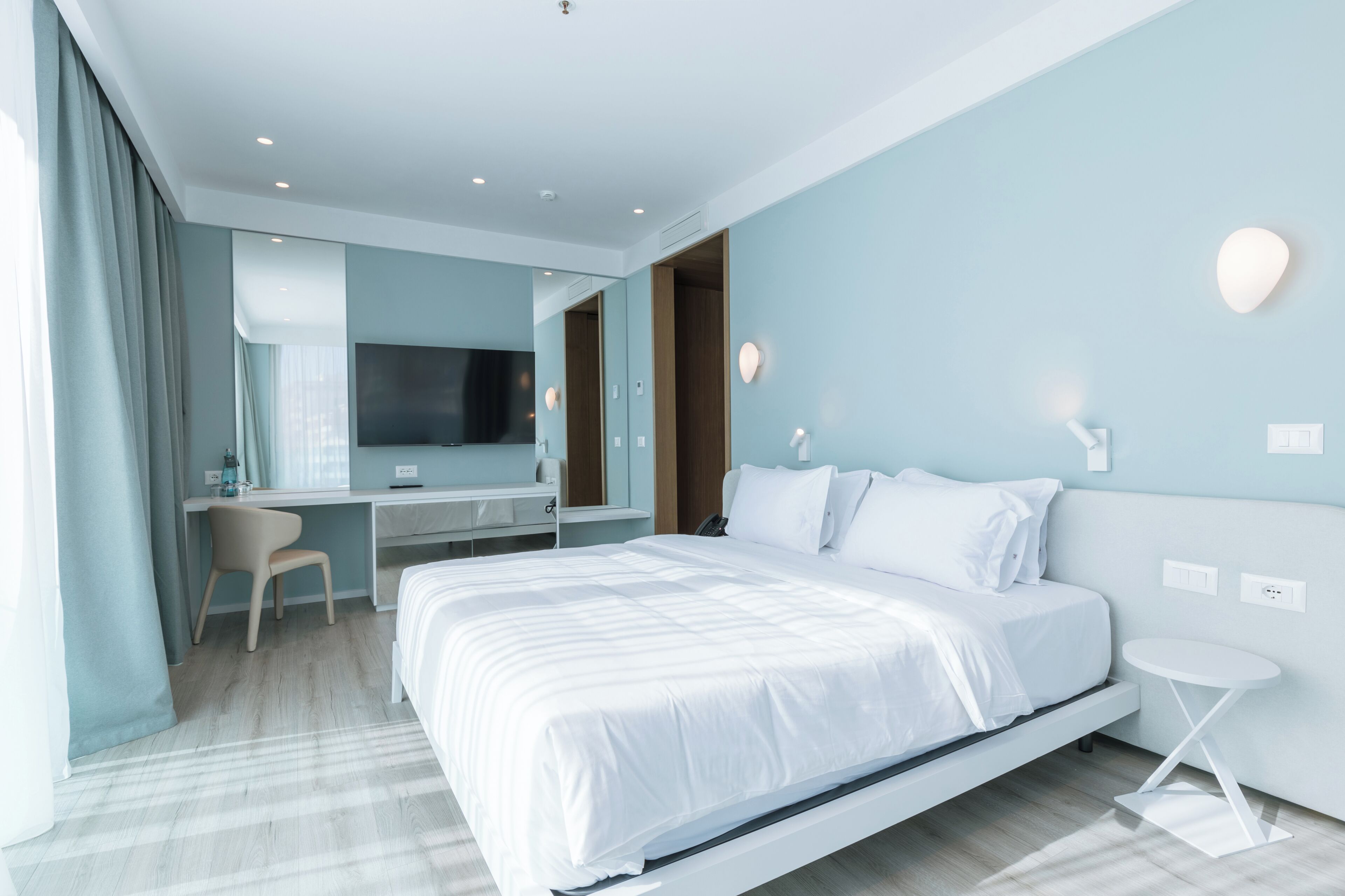 A modern hotel room with a large bed, a desk, a chair, and a TV.