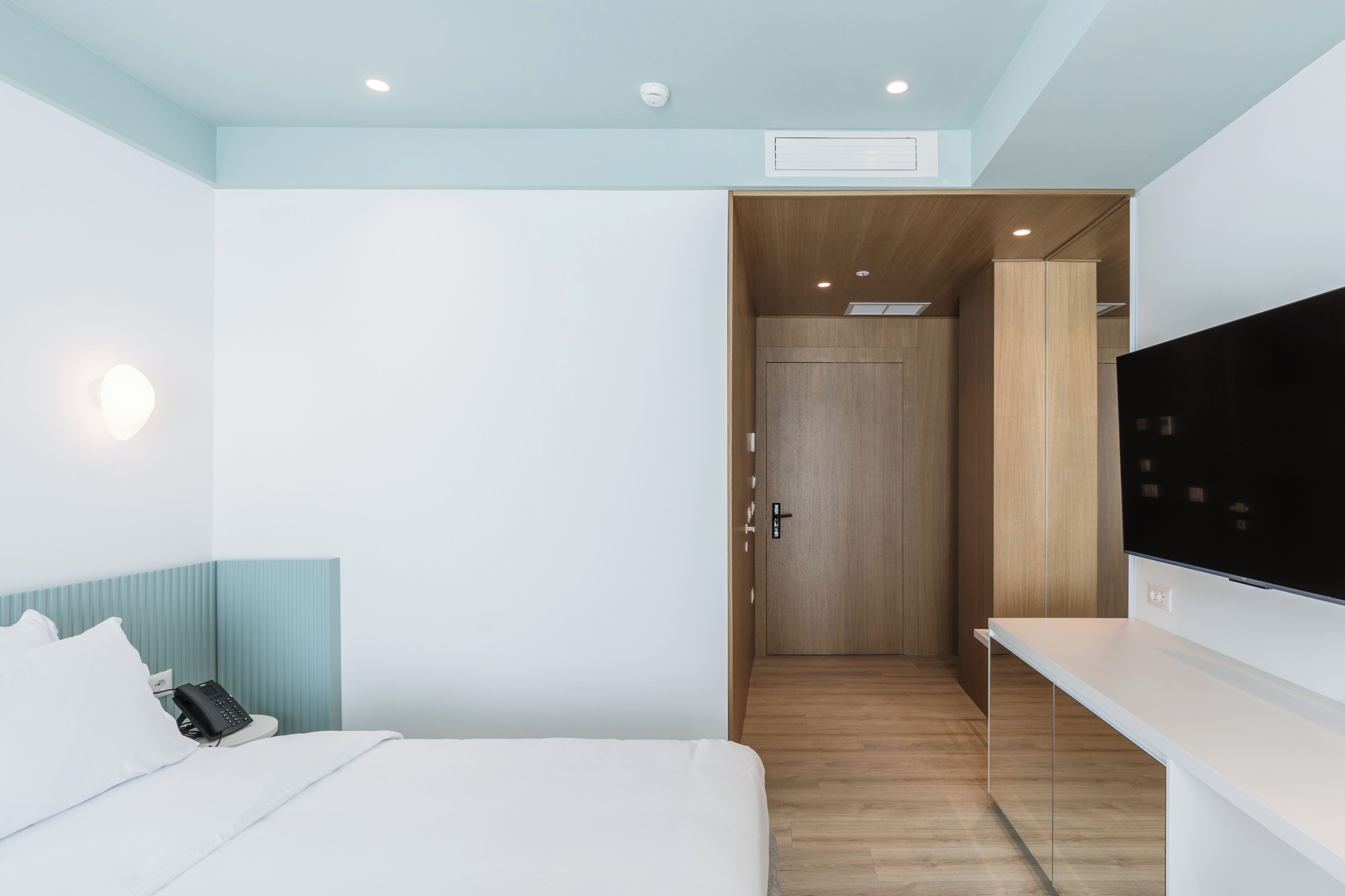 Une chambre d’hôtel avec un lit, un téléphone sur la table de chevet, une télévision et une armoire en bois.
