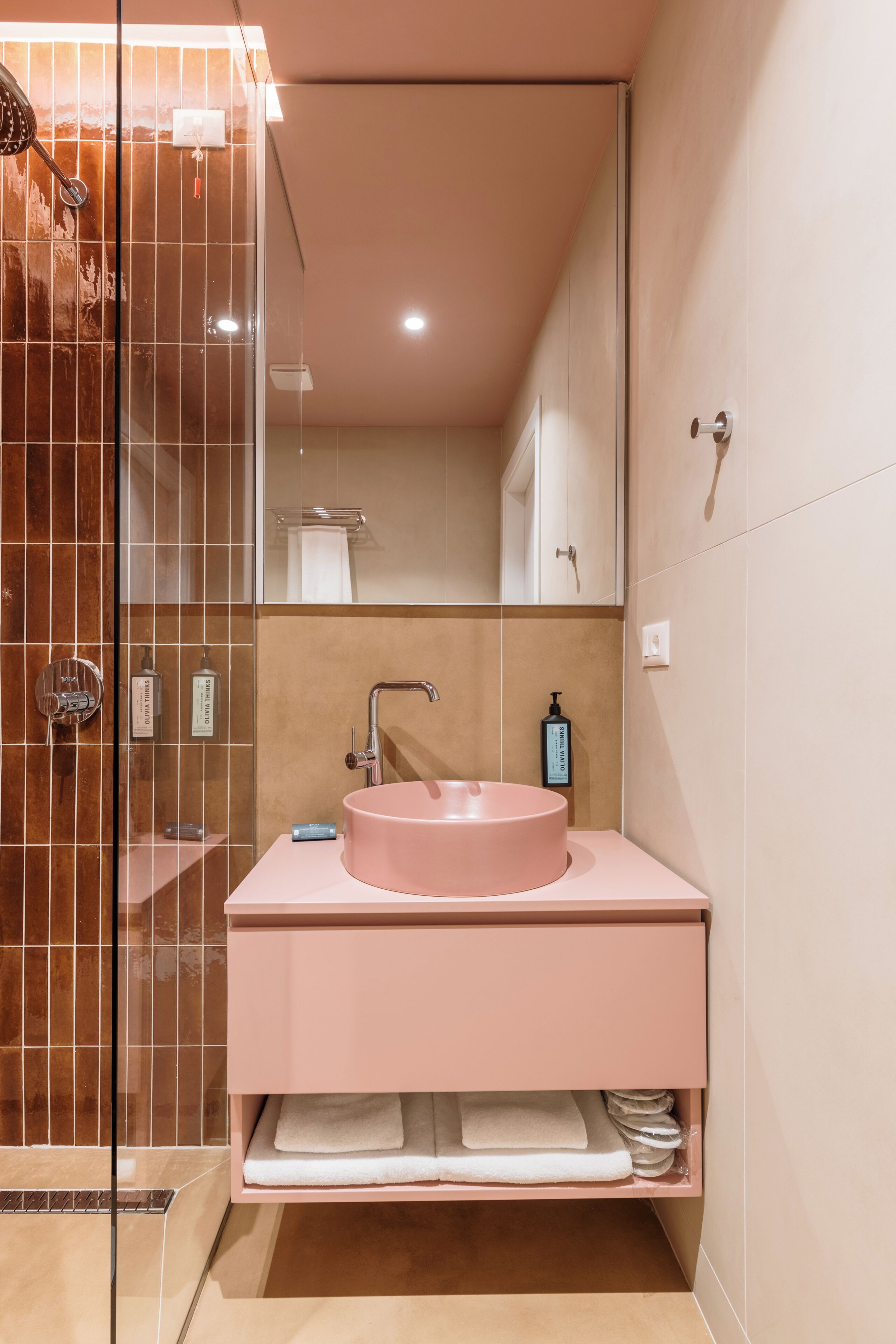 A bathroom with a glass shower enclosure, a pink sink, and a mirror above it.