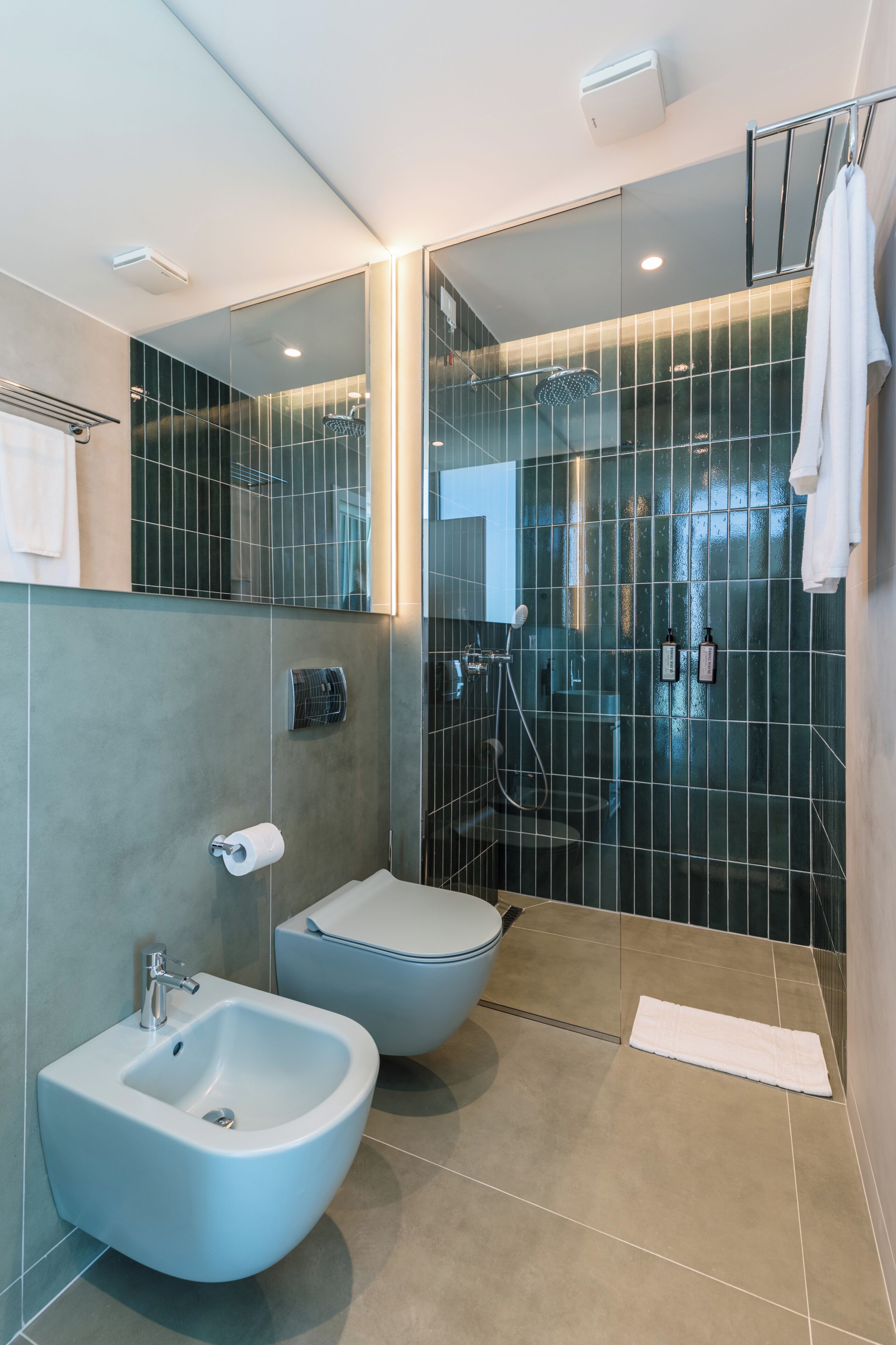 Un baño moderno con un bidé, un inodoro, una cabina de ducha de vidrio y un perchero para toallas.