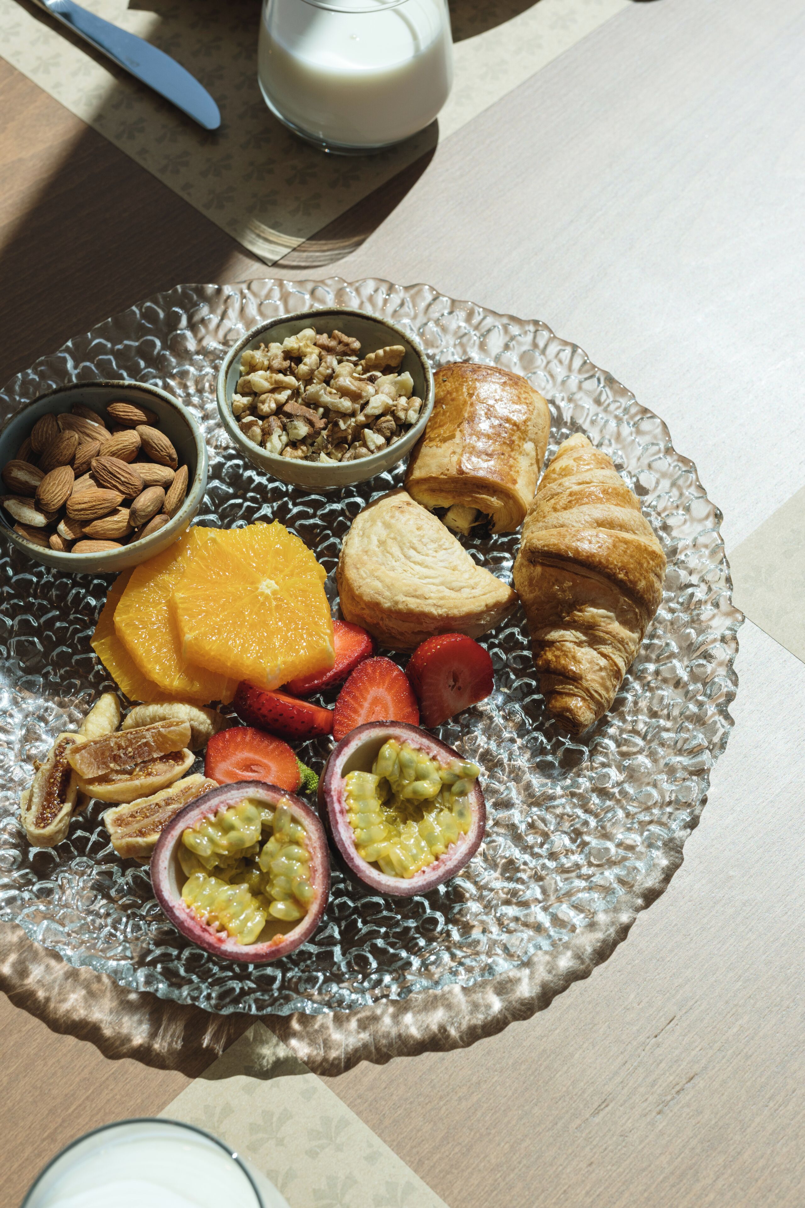 A glass plate with assorted snacks and a glass of milk on a table.