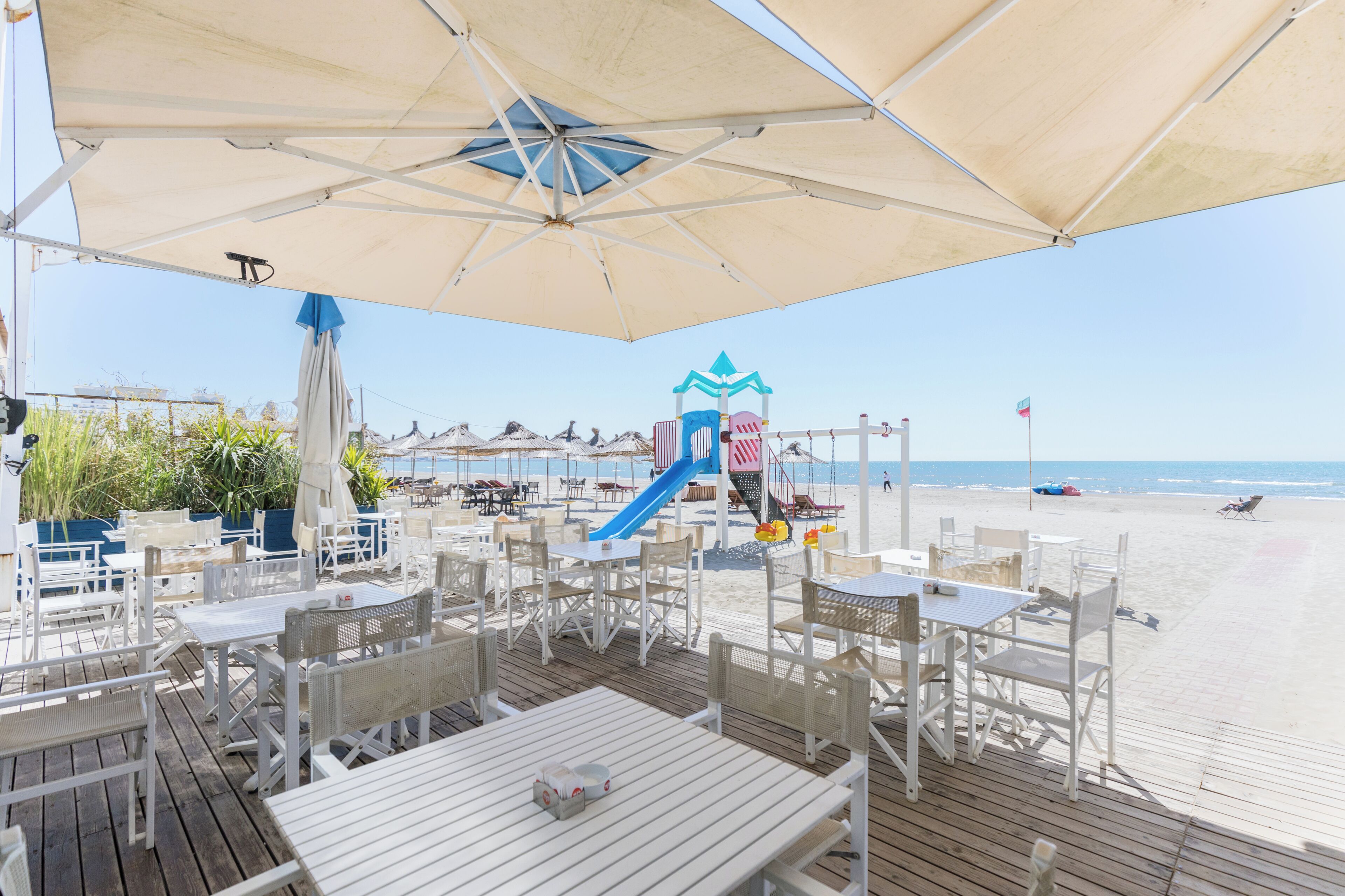 Un espacio exterior con mesas y sillas para comer, un tobogán y vistas a la playa.