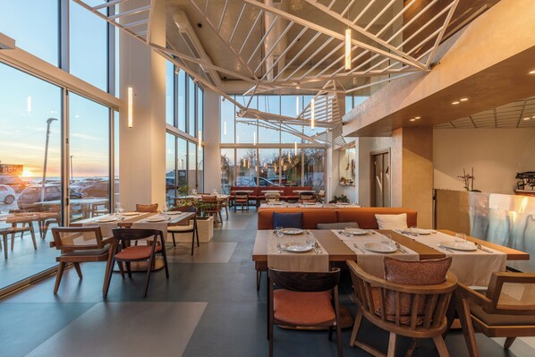 A spacious restaurant with high ceilings, large windows, and a view of the cityscape. - Nava Star Hotel (Durrës)