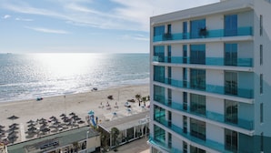 Un hotel de varios pisos con balcones que dan a la playa, una zona de piscina y vistas despejadas al océano.