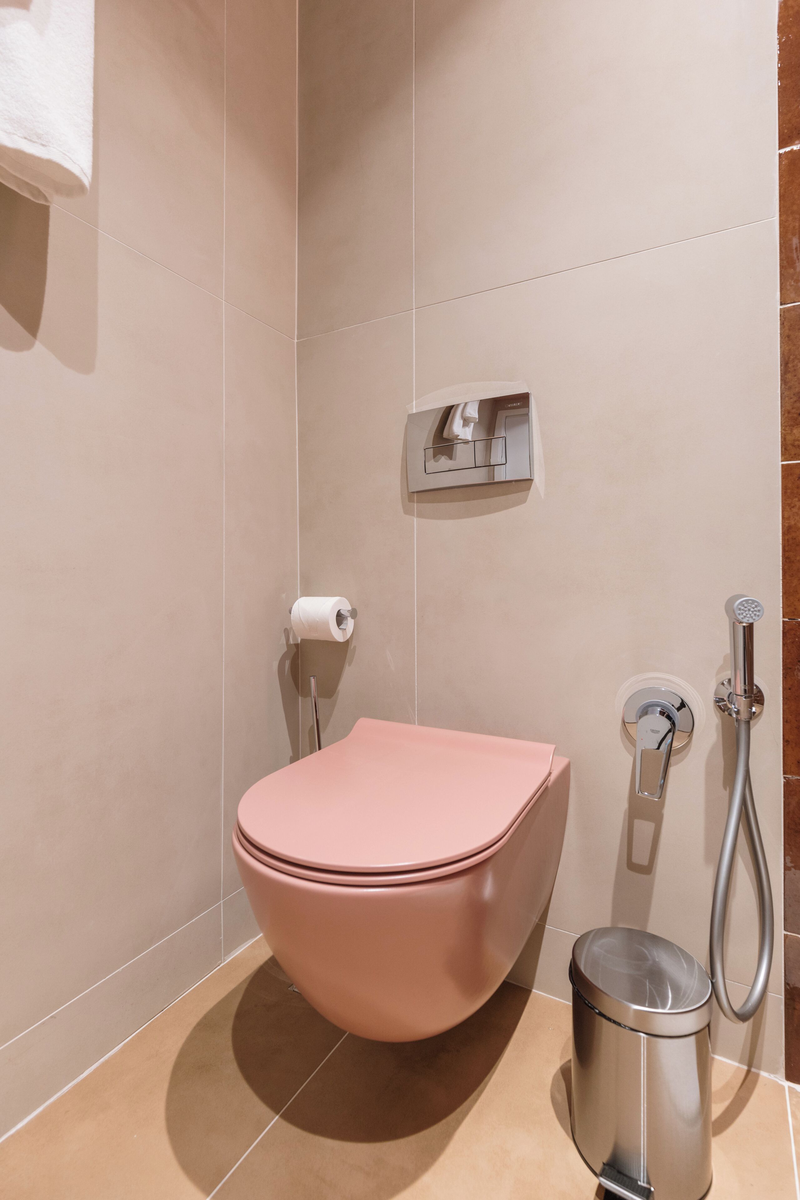 Une salle de bain avec des toilettes roses, une poubelle, un distributeur de serviettes et une pomme de douche.