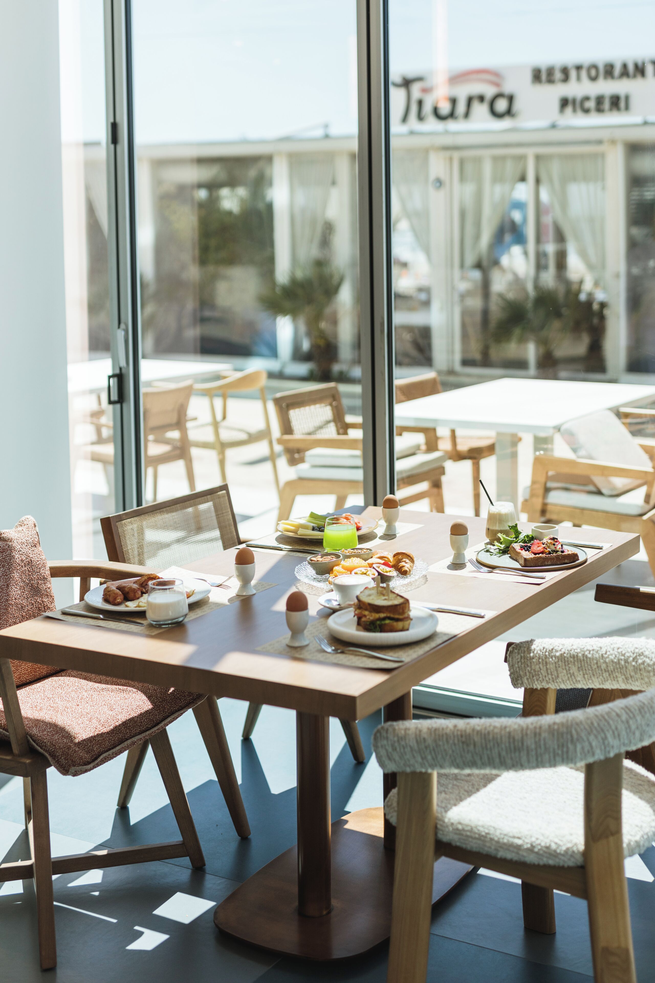 A dining area with tables, chairs, and a view of a restaurant named 'Tiara Pizzeria' through large windows.