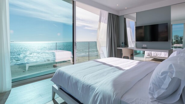 Habitación de hotel moderna con una cama grande, televisión y balcón con vista al mar.