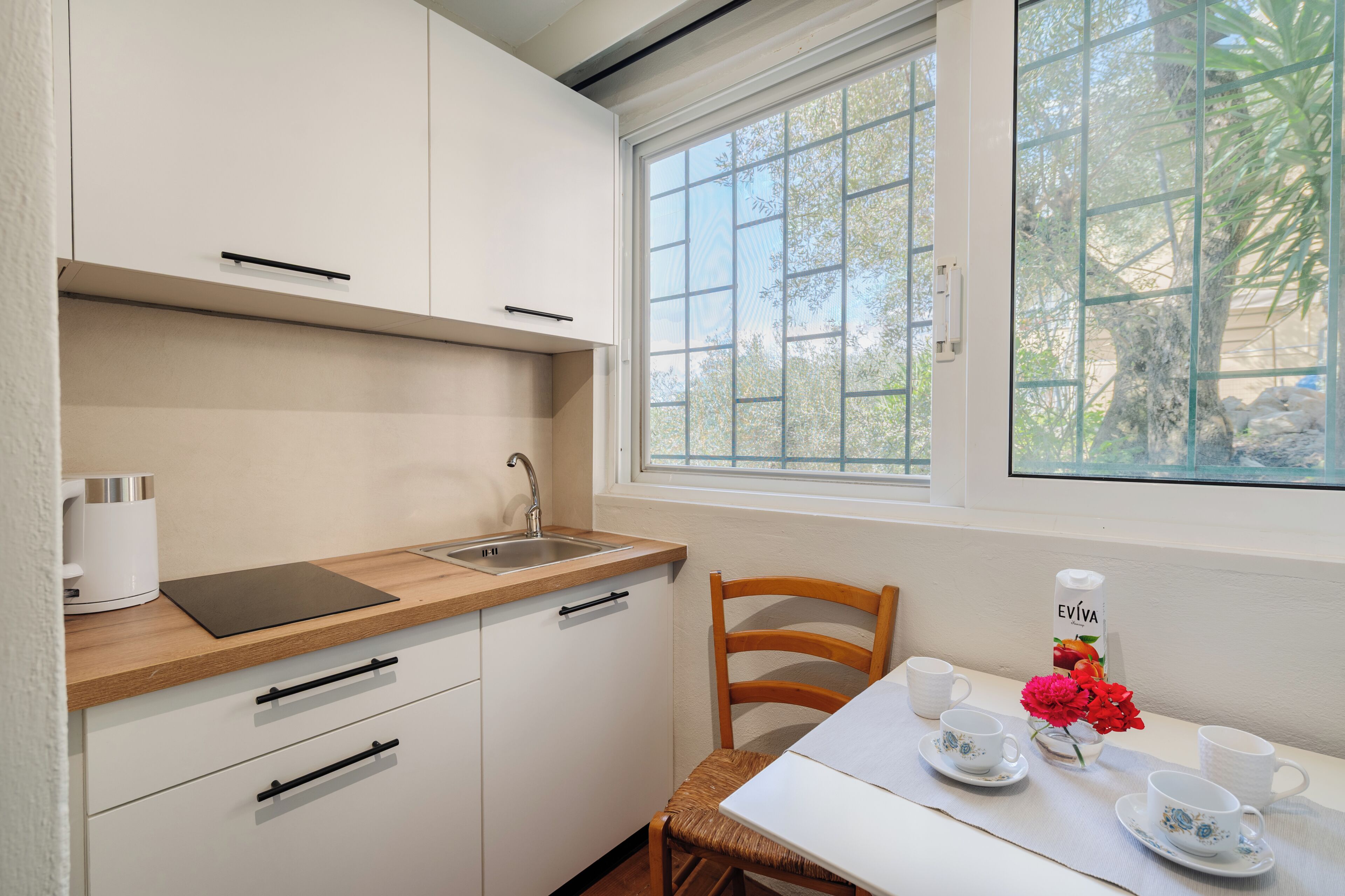 Una cocina compacta con ventana, un lavamanos y una zona de comedor con una mesa preparada para dos.