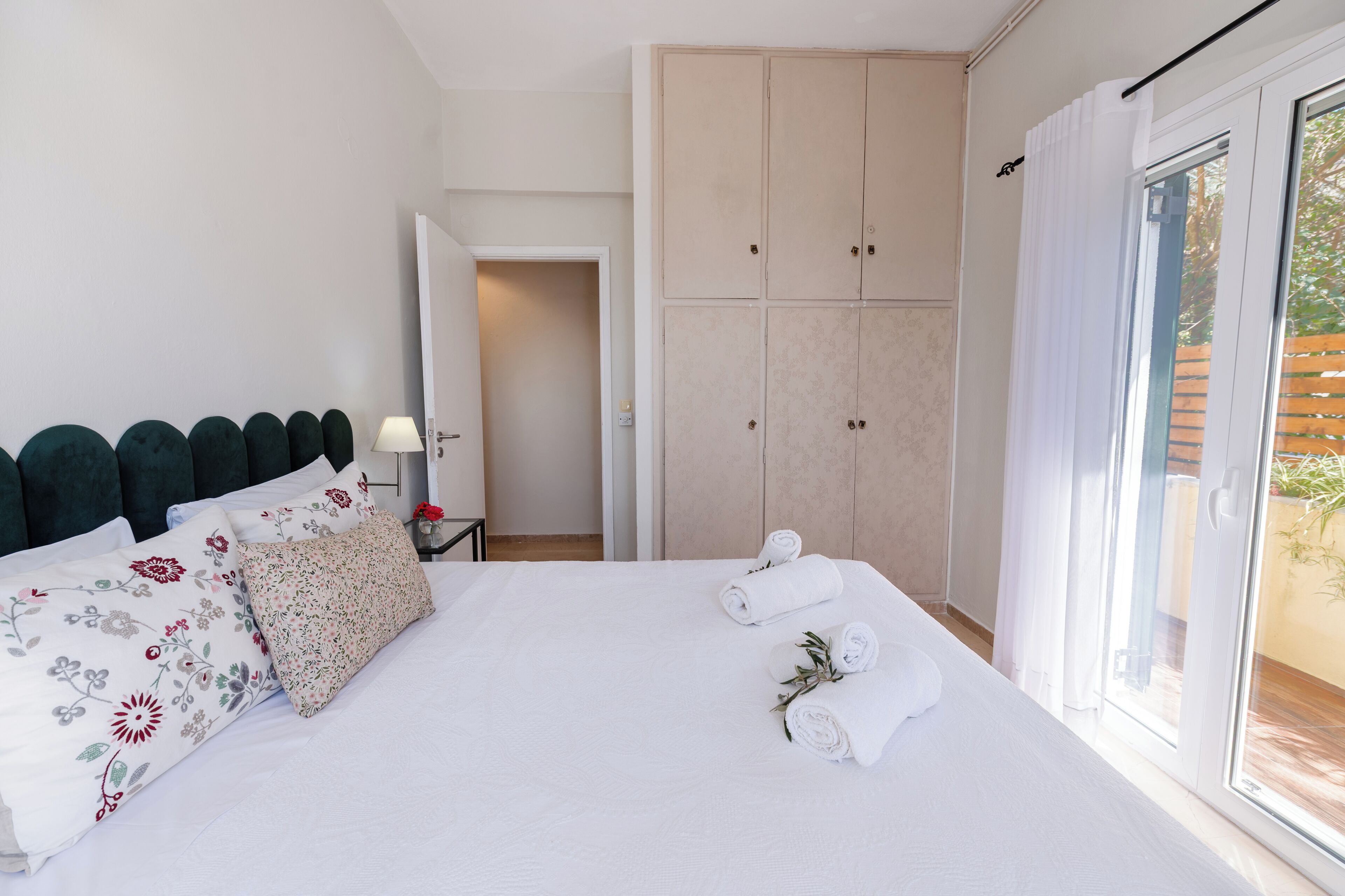 A hotel room with a bed, a wardrobe, a nightstand, and a view through a sliding door.