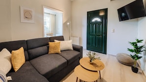 Un salón con un sofá gris oscuro, una mesa de centro redonda de madera, una puerta verde y un televisor montado.