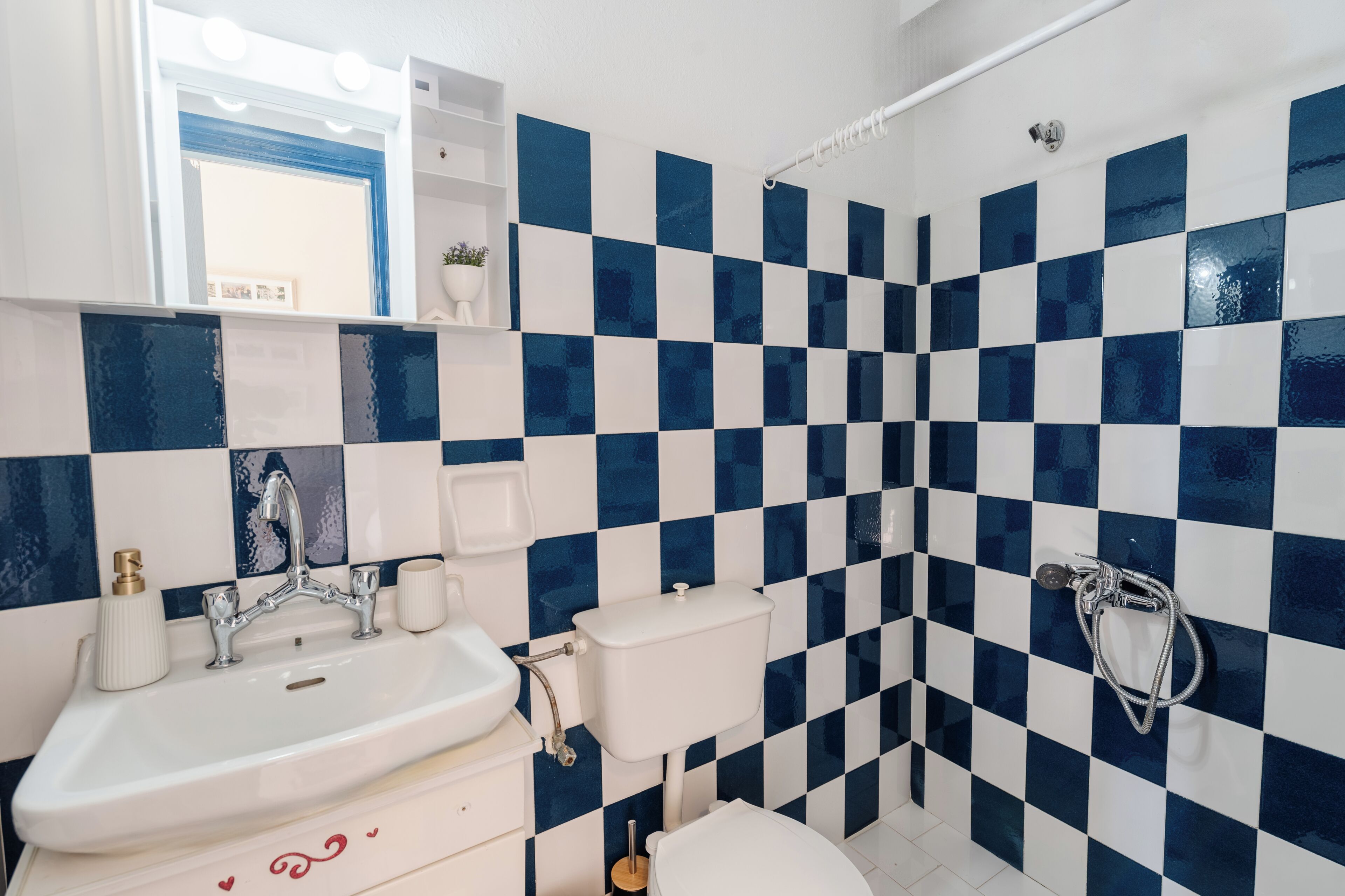 A bathroom with a checkered tile pattern, a sink, a toilet, and a shower.