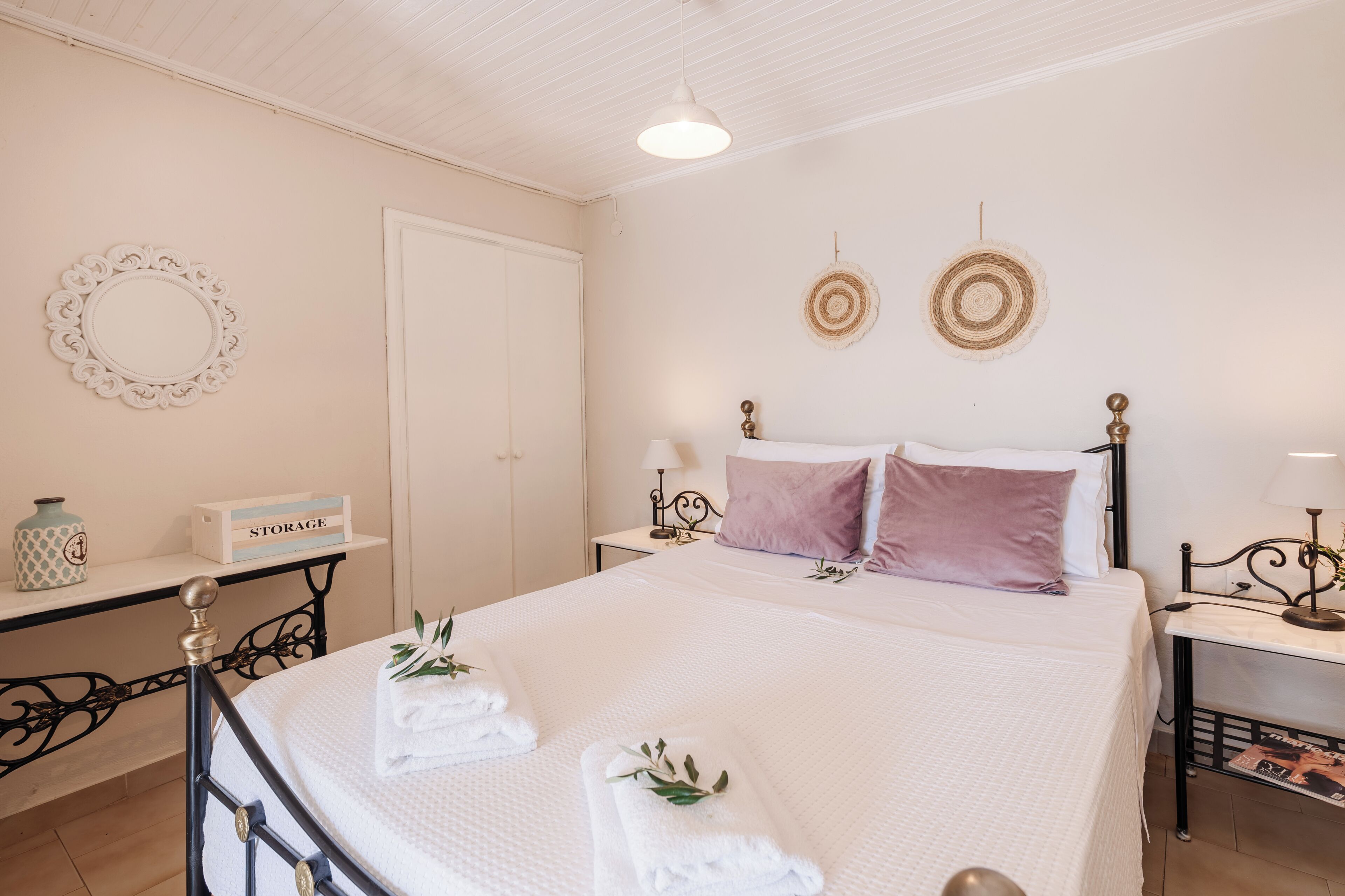 Een netjes opgemaakt slaapkamer met een bed, nachtkastjes, een opbergkist en decoratieve wandobjecten.