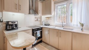 Una cocina moderna con armarios de madera, una campana extractora de acero inoxidable, una mesa de vidrio y un ventanal con cortinas.