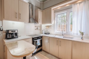 Una cucina moderna con mobili in legno, una cappa aspirante in acciaio inox, un tavolo in vetro e una finestra con tende.