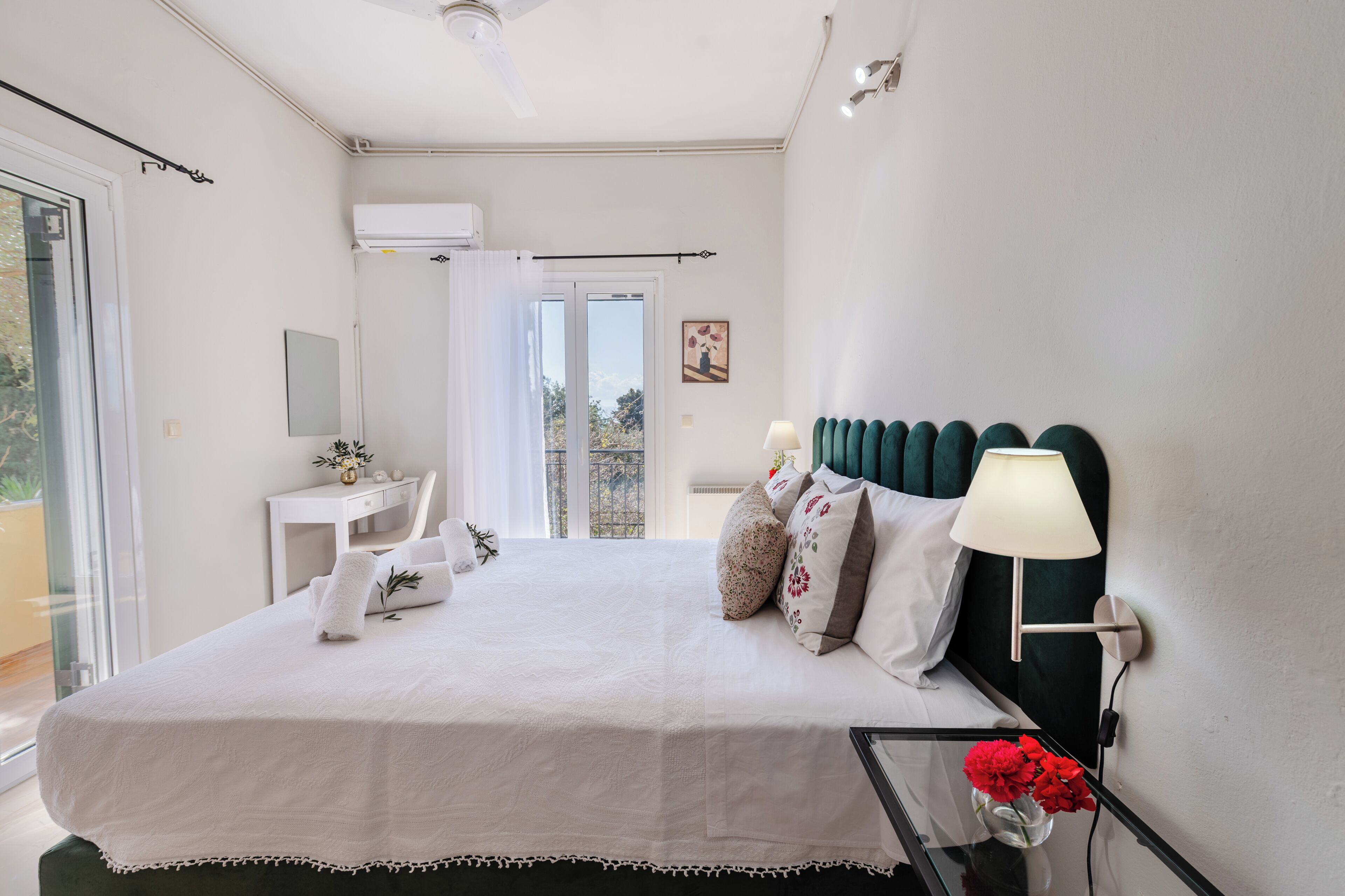 A bedroom with a bed, bedside table, lamp, and a view of the outdoors.