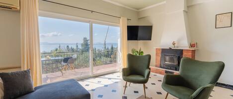 A living room with a sofa, two armchairs, a fireplace, a TV, and a balcony with a view.