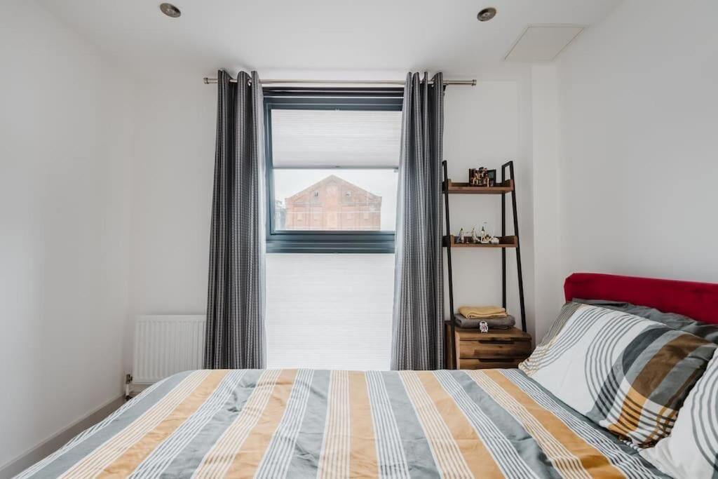 Ein Schlafzimmer mit Bett, Fenster mit Vorhängen, Heizkörper und Ablagefläche mit Gegenständen.