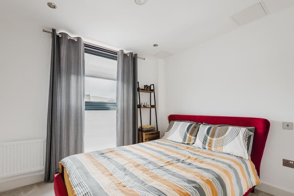 A bedroom with a bed, curtains, a nightstand, and a view of the outdoors.