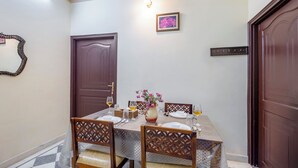 A dining area with a table set for four, chairs, a vase with flowers, and a wall-mounted picture. - Alaya Stays Abhimanyu Mansion Topaz 2BHk (Udaipur)