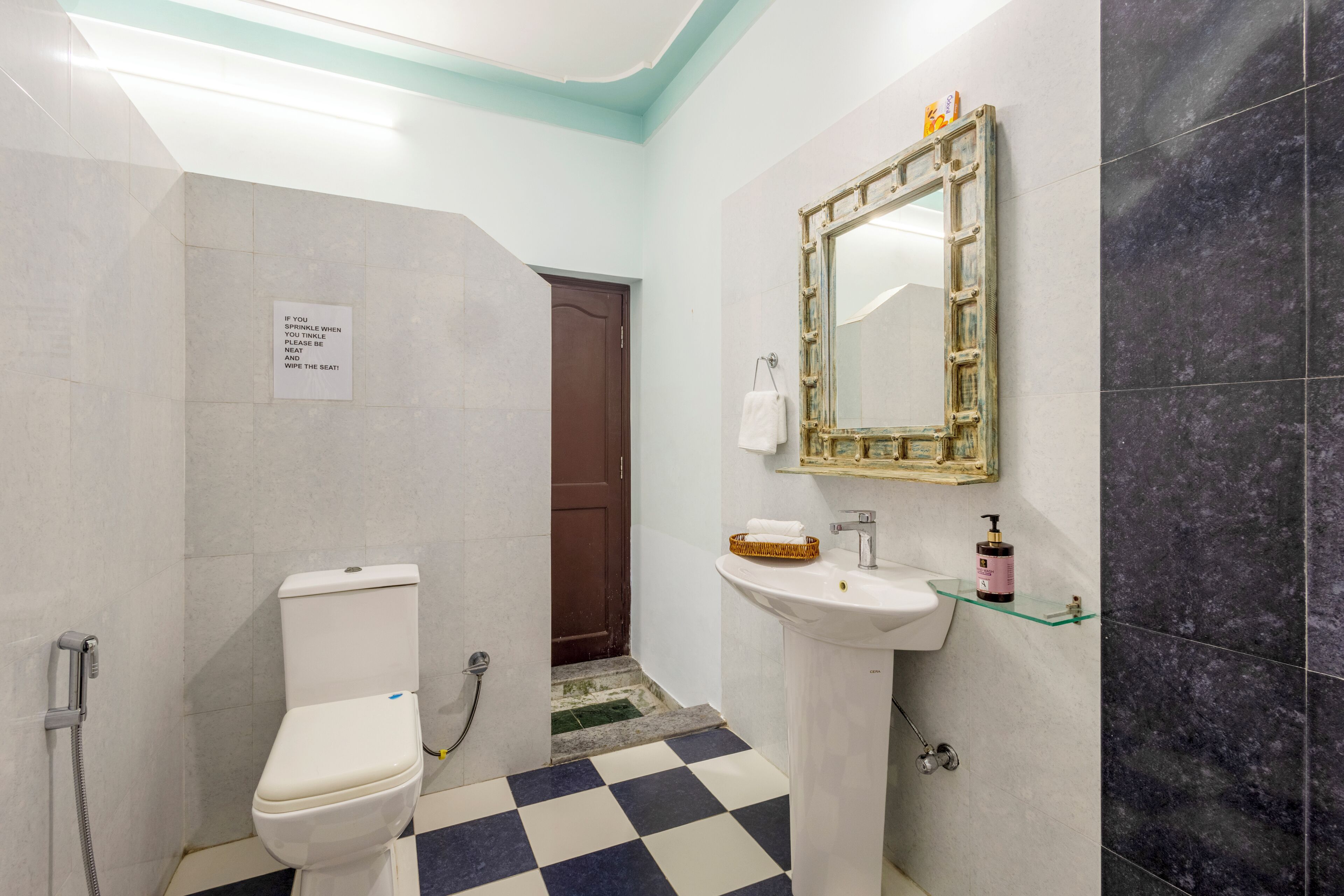 Un baño con inodoro, lavabo, espejo y un cartel en la pared.