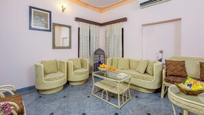 A living room with wicker furniture, a glass coffee table, and a framed picture on the wall. - Alaya Stays Abhimanyu Mansion Topaz 2BHk (Udaipur)