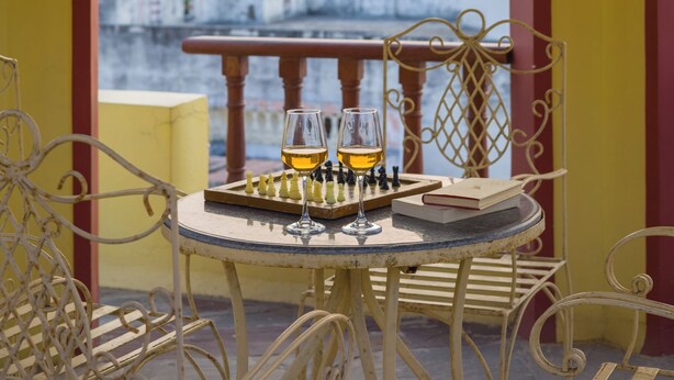 A balcony with a table, chairs, a chessboard, and a glass of wine. - Alaya Stays Abhimanyu Mansion Topaz 2BHk (Udaipur)