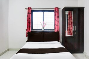 Una camera da letto con un letto, una finestra con tende, una porta scura e un vaso con fiori.