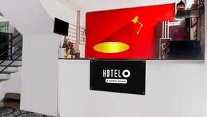 A hotel reception area with a red wall, a black sign reading 'HOTELO Company Serviced,' and a staircase to the left. - Classic With Twin Bedspot Light Lodging (Pune)