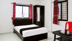 A bedroom with a bed, a wardrobe, a table with a kettle, and a window with curtains. - Classic With Twin Bedspot Light Lodging (Pune)