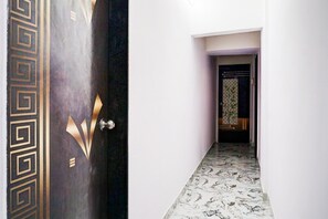 A hallway with a patterned door, a tiled floor, and a view into a room with a patterned wall. - Classic With Twin Bedspot Light Lodging (Pune)