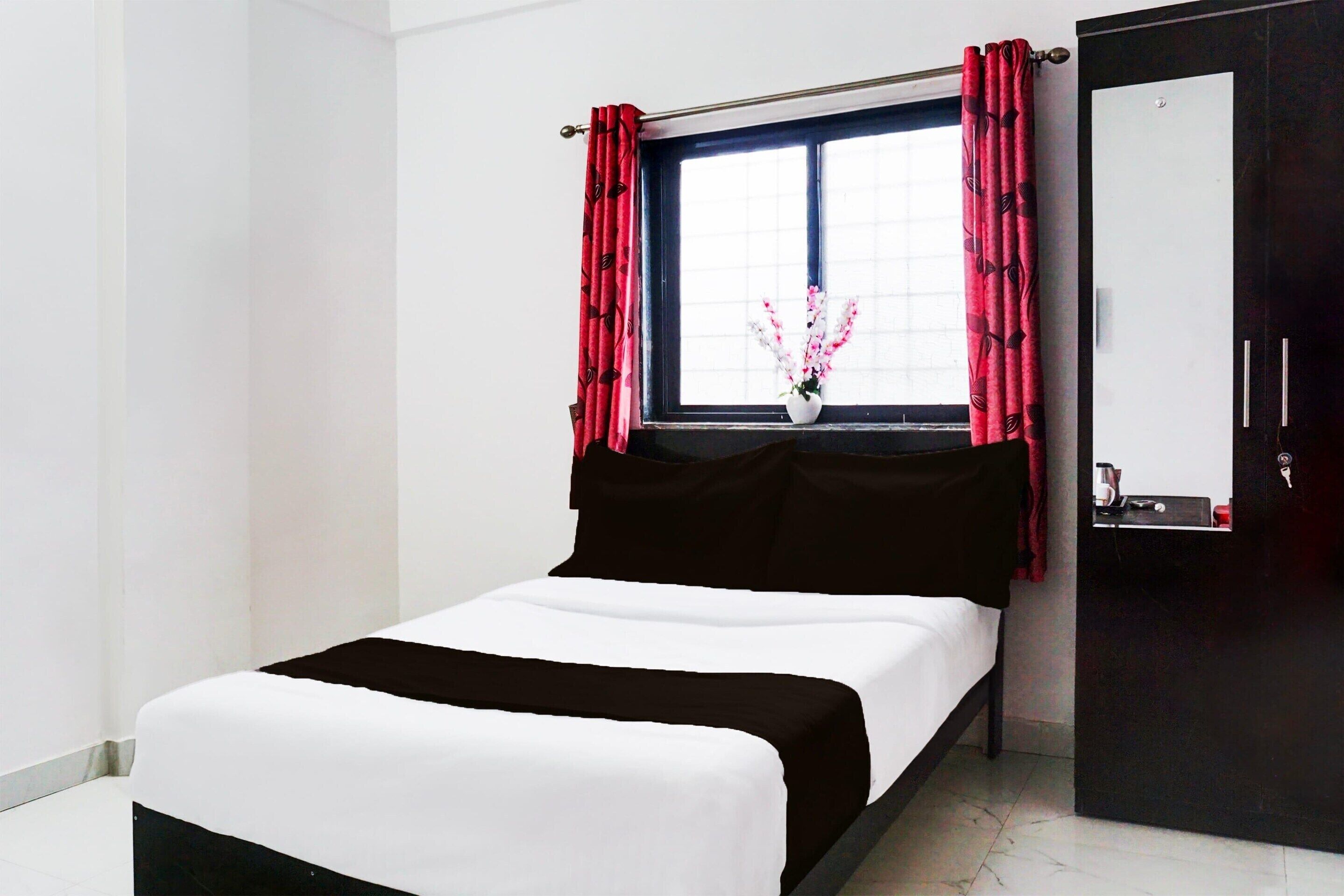 A room with a bed, a window with curtains, a mirror, and a wardrobe.
