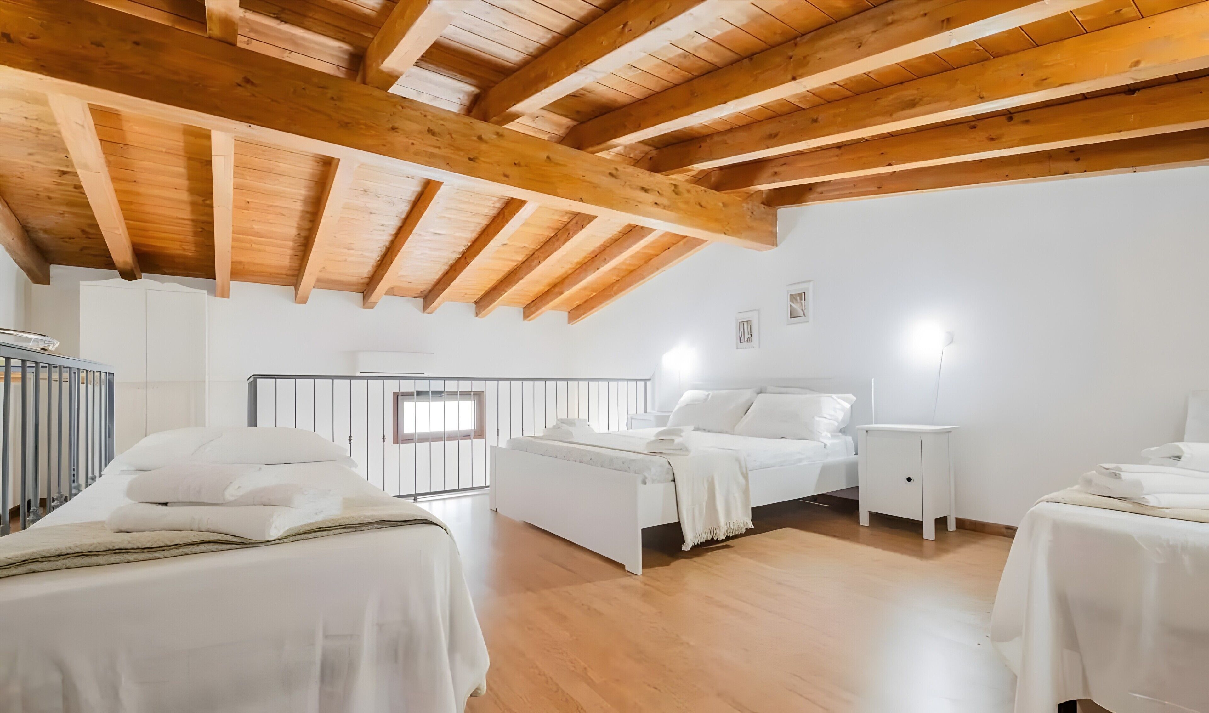 A room with wooden beams, a bed, a bedside table, a nightstand, and a window.