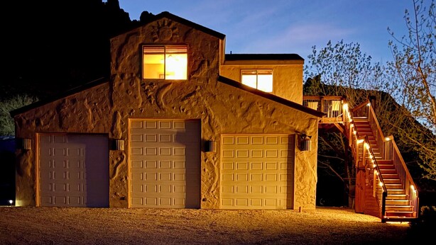 Un edificio de piedra con dos puertas de garaje, una escalera y un ventanal pequeño.