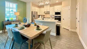 A modern kitchen with white cabinets, stainless steel appliances, and a wooden dining table set for four. - Brand New Home at Reunion Resort - Near Disney (Kissimmee)
