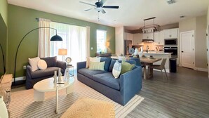 A living room with a sofa, coffee table, and lamp; a dining area with chairs and a table; and a kitchen with cabinets and appliances. - Brand New Home at Reunion Resort - Near Disney (Kissimmee)