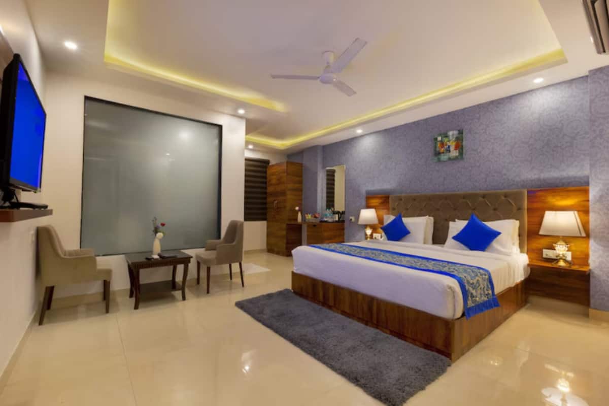 Une chambre d’hôtel avec un grand lit, un bureau, une chaise, une télévision et un ventilateur de plafond.