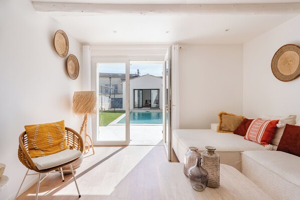 A modern living room with a sofa, a wicker chair, a lamp, and a view of a swimming pool. - Les Terrasses du Ventoux - Garage & Swimming pool (Bédoin)