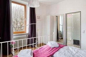 Makuuhuone, jossa on sänky, ikkuna verhoilla, patteri ja ovi, joka johtaa kylpyhuoneeseen.