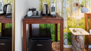 A kitchenette with a coffee maker, kettle, and toaster on a wooden table, a refrigerator below, and a wall with a nature wallpaper. - Room “Birke” with Shared Garden and Wi-Fi (Vogtsburg im Kaiserstuhl)
