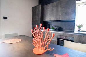 Une cuisine moderne avec un élément central orange original, un four encastré et une fenêtre agrémentée d’une plante.