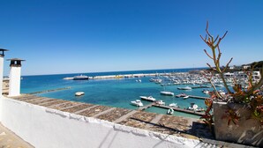 A coastal marina with boats docked, a clear blue sky, and a white building with a stone base. - C-Home Otranto – Design Apartment with Panoramic Terrace (Otranto)
