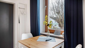 Een kamer met een houten tafel, witte stoelen, een raam met gordijnen en een vaas met bloemen.