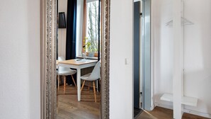 Een kamer met houten vloer, een eettafel met stoelen, een raam met gordijnen en een witte deur.