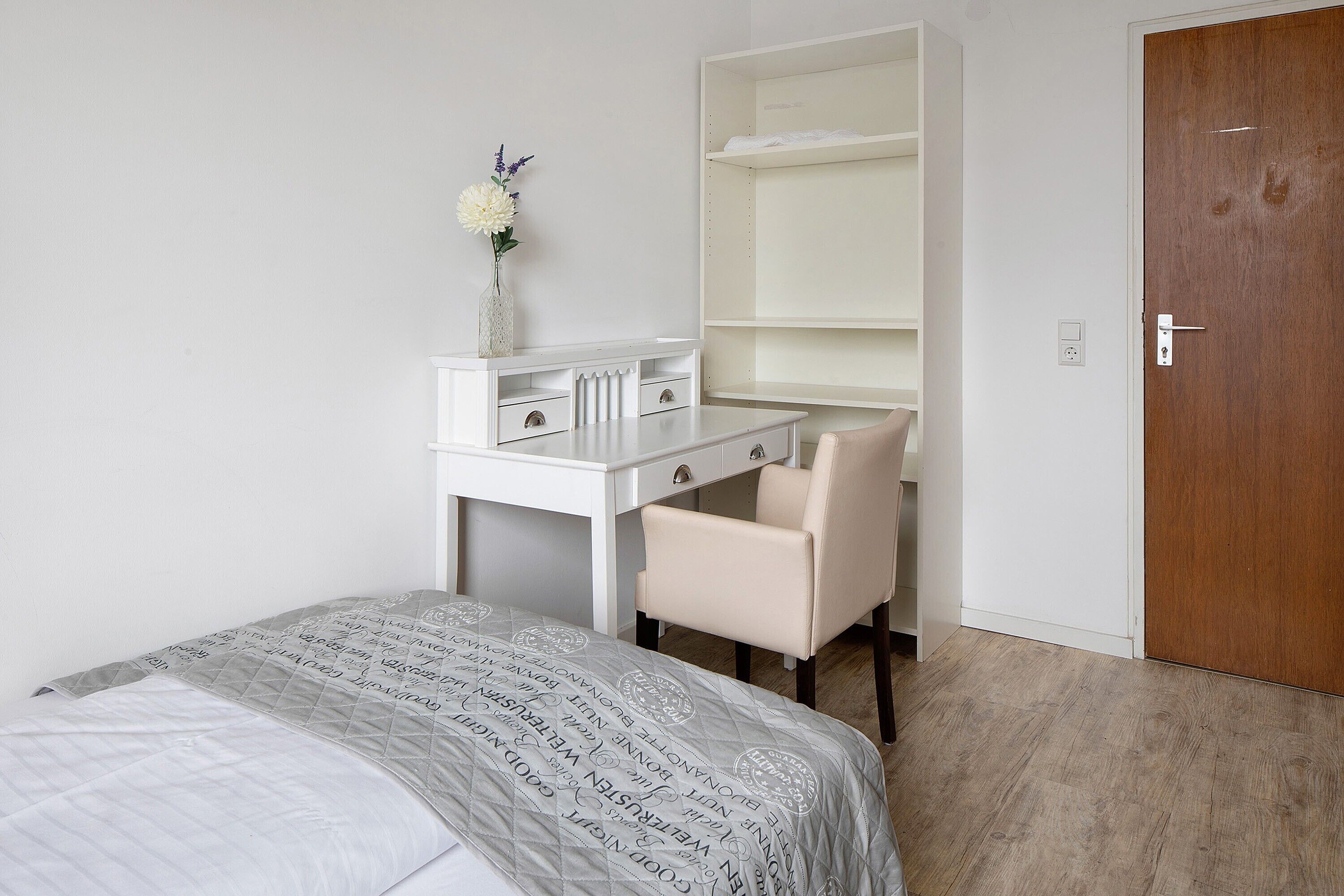 Un dormitorio con cama, escritorio, silla, armario y puerta.