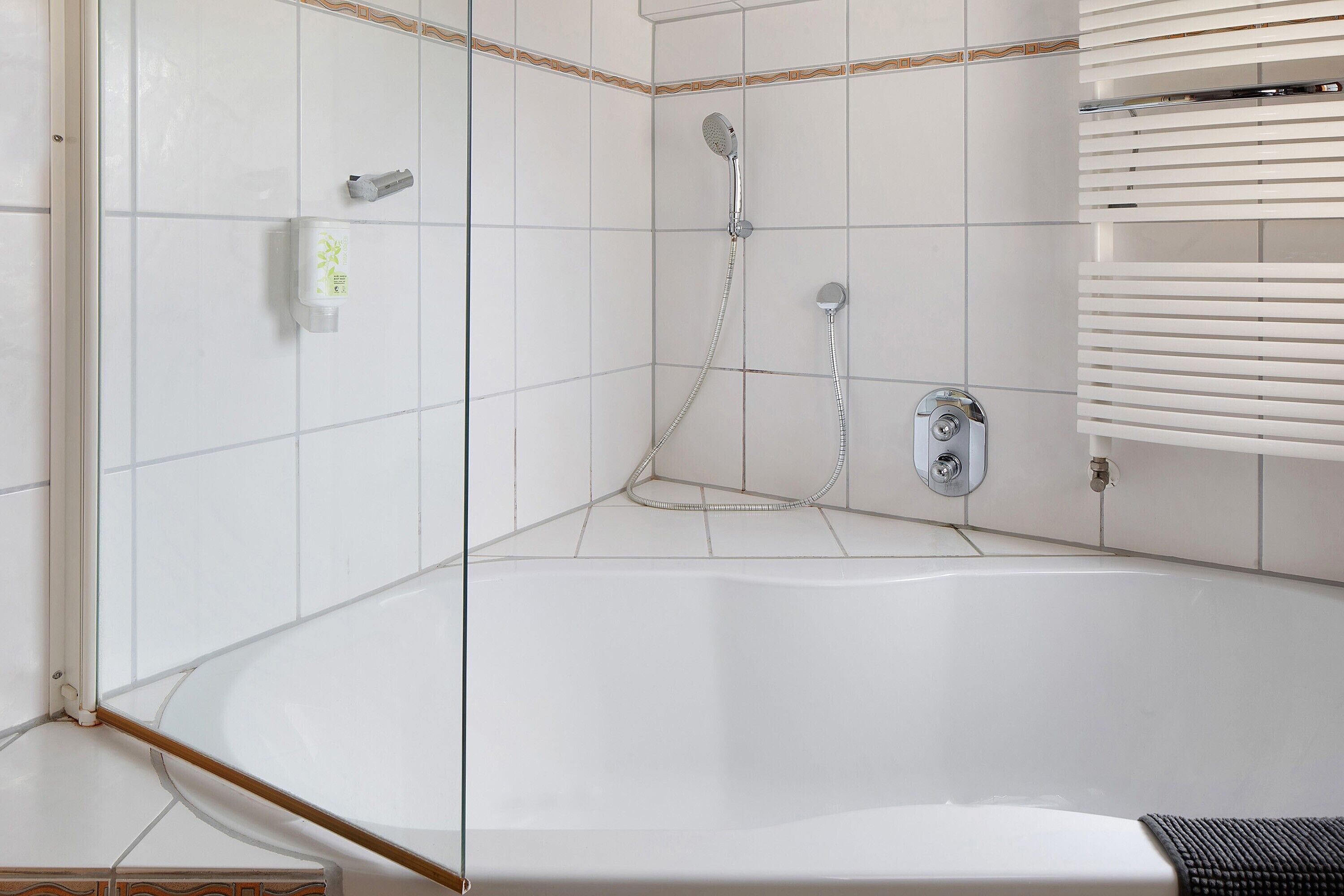 Un baño en esquina con bañera, cabezal de ducha y secador de manos.