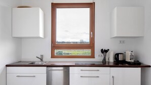 Uma cozinha com armários brancos, uma geladeira de aço inoxidável, bancada de madeira e janela com vista para uma paisagem verde.