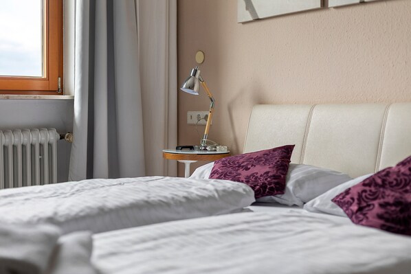 A hotel room with a bed, a nightstand, a lamp, and a window.