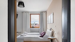 Ein Schlafzimmer mit einem Bett, einem Fenster, einem Heizkörper, einer Lampe und einem kleinen Tisch.