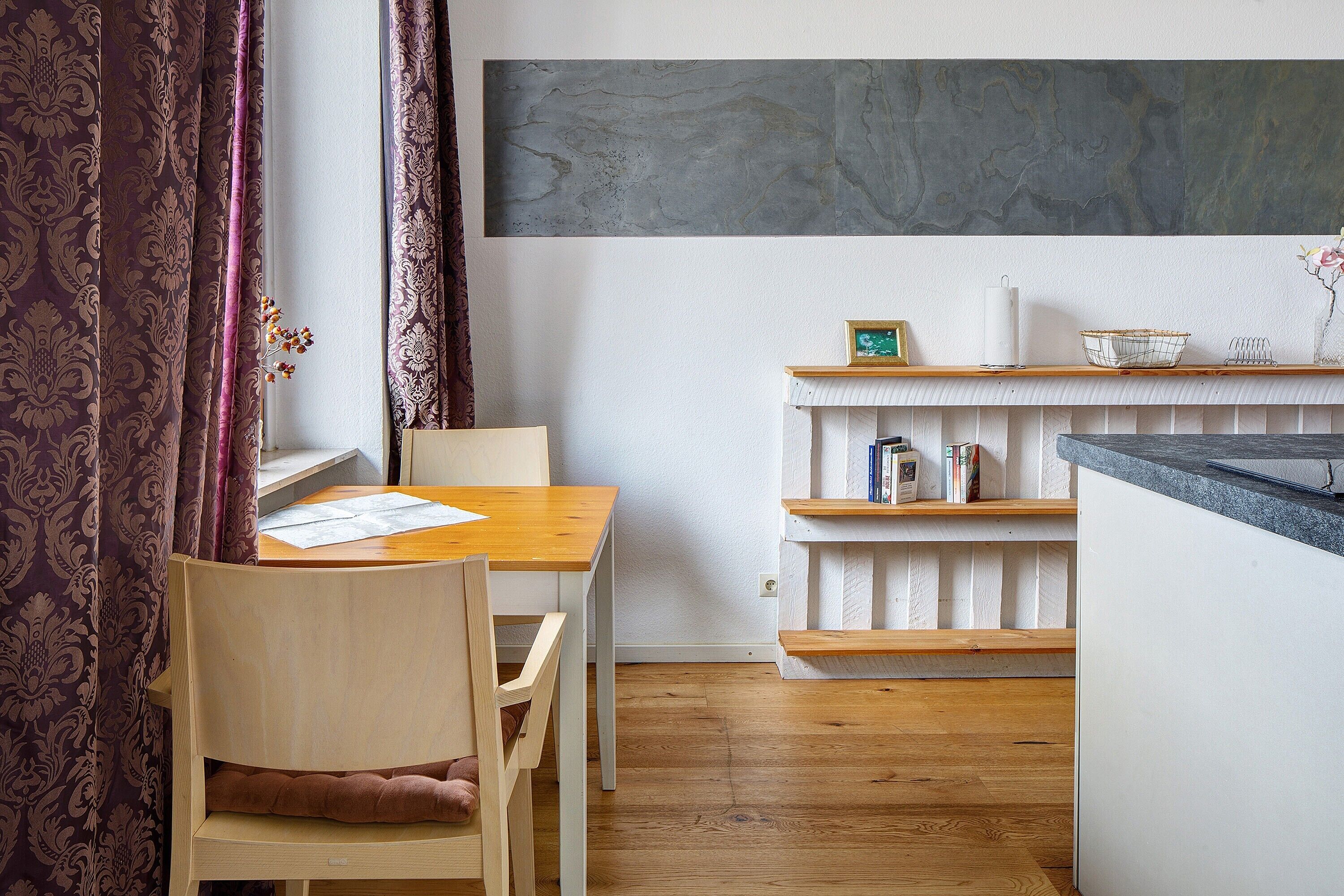 Une pièce comprenant une table à manger en bois, une chaise, une bibliothèque et un comptoir de cuisine.