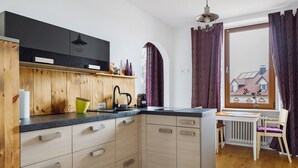 Una cocina moderna con armarios de madera, encimera negra y ventana con cortinas moradas.